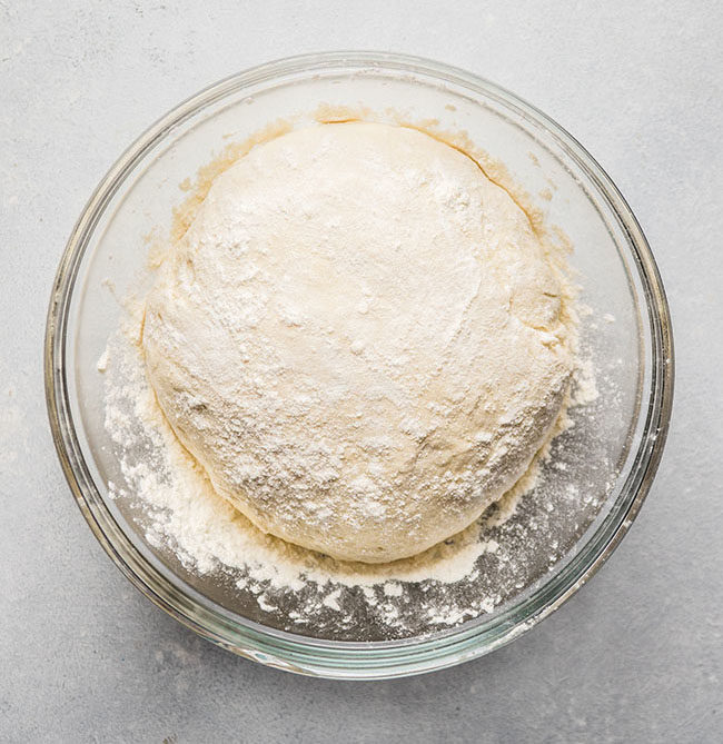 overhead photo of bread dough in a glass bowl on a white countertop